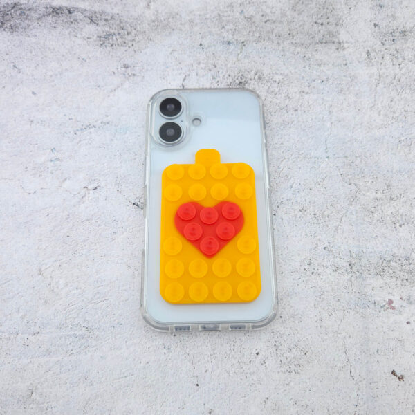 Orangefarbener Noppie-Heart-Patch mit rotem Herz auf transparenter Handyhülle, modernes Smartphone Accessoire mit Saugnäpfen auf beiden Seiten